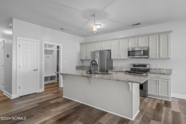 kitchen with light stone countertops, stainless steel appliances, dark hardwood / wood-style floors, a breakfast bar area, and a center island with sink