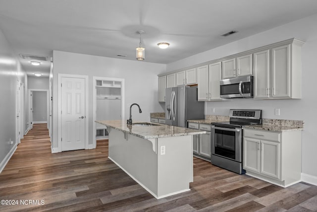 kitchen with appliances with stainless steel finishes, light stone counters, a kitchen island with sink, dark wood-type flooring, and sink