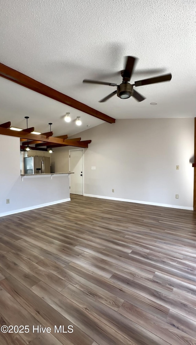 unfurnished living room featuring wood-type flooring, vaulted ceiling with beams, a textured ceiling, and ceiling fan