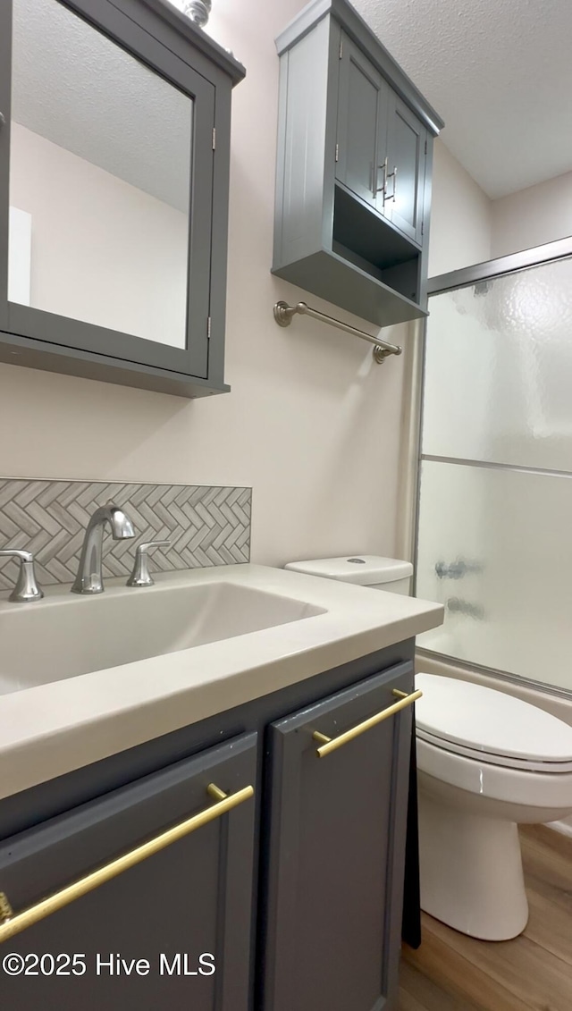 full bathroom featuring combined bath / shower with glass door, decorative backsplash, vanity, hardwood / wood-style flooring, and toilet