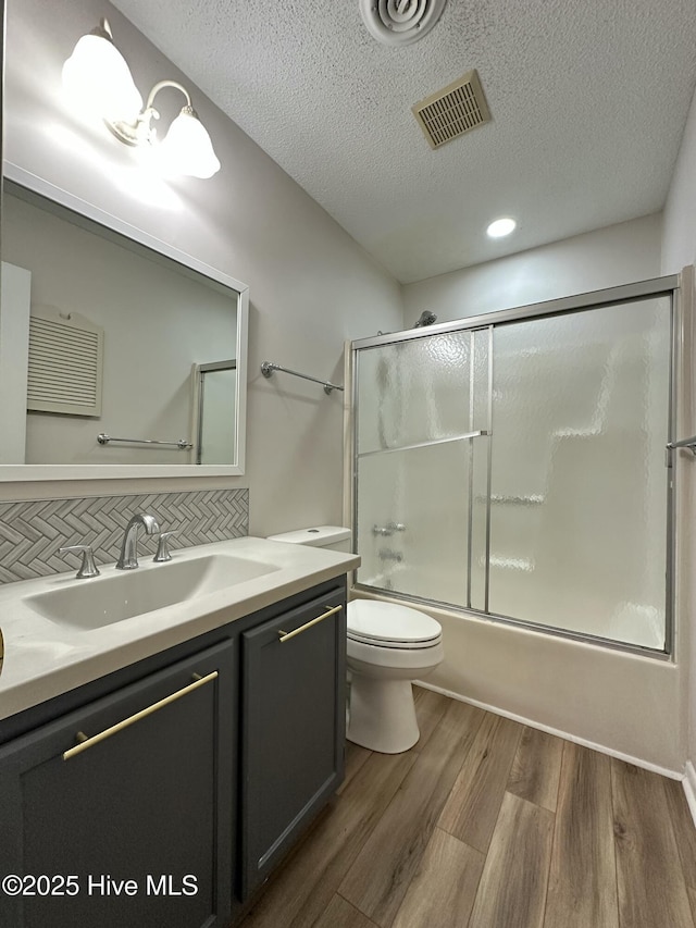 full bathroom featuring combined bath / shower with glass door, wood-type flooring, toilet, decorative backsplash, and vanity