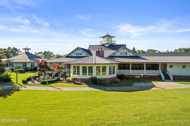 back of property with a standing seam roof, a chimney, a yard, and metal roof
