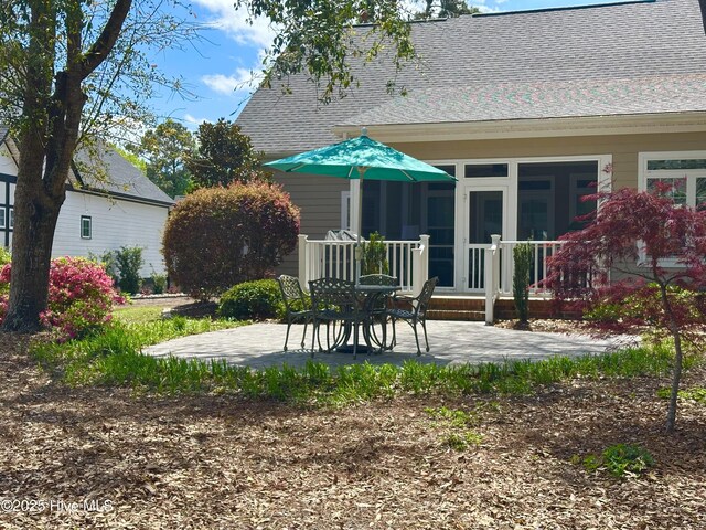 rear view of property featuring a sunroom, a shingled roof, and a patio area