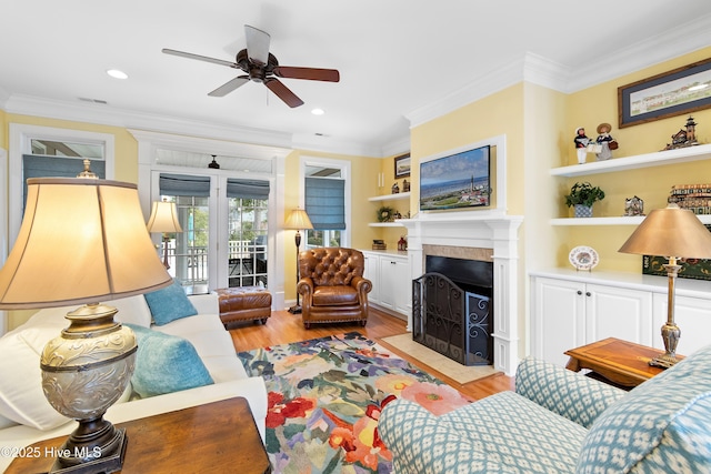 living area with crown molding, ceiling fan, light wood finished floors, recessed lighting, and a fireplace with flush hearth