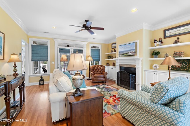 living area featuring ceiling fan, a fireplace with flush hearth, crown molding, light wood finished floors, and recessed lighting