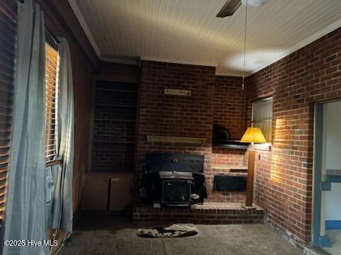 living room featuring crown molding, brick wall, a wood stove, and ceiling fan