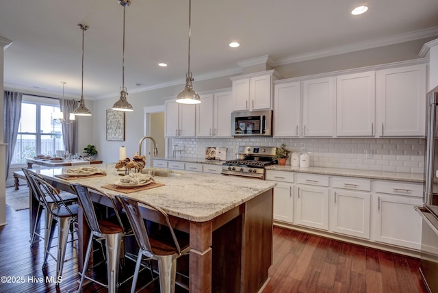 kitchen featuring stainless steel appliances, sink, decorative light fixtures, white cabinetry, and an island with sink