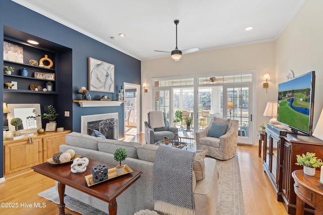 living room with french doors, light hardwood / wood-style floors, built in features, ceiling fan, and crown molding