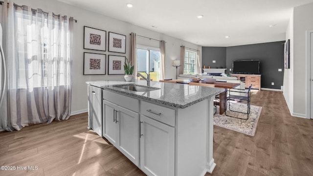 kitchen featuring light wood-type flooring, light stone counters, sink, a center island with sink, and white cabinets