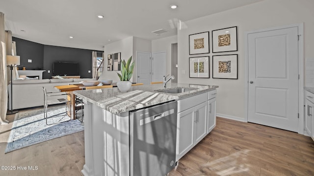 kitchen with dishwasher, sink, light stone counters, an island with sink, and white cabinets