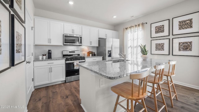 kitchen with white cabinetry, sink, light stone counters, a breakfast bar area, and appliances with stainless steel finishes