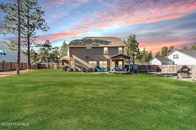 back house at dusk with a patio area and a lawn