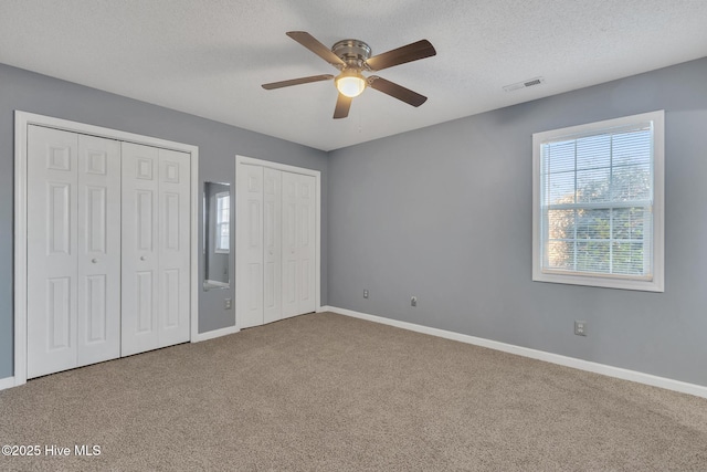 unfurnished bedroom featuring a textured ceiling, ceiling fan, carpet flooring, and two closets