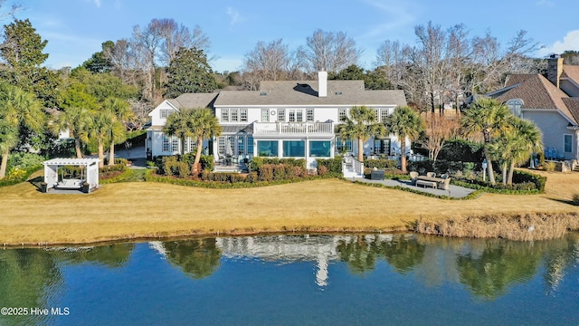 back of property with a balcony, a pergola, a water view, and a yard