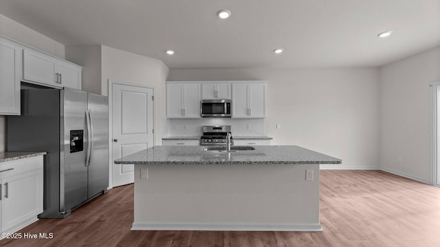 kitchen featuring light stone countertops, a center island with sink, white cabinets, and stainless steel appliances