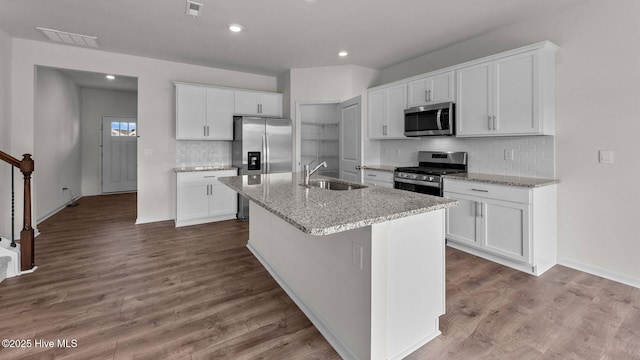 kitchen featuring white cabinets, sink, light stone countertops, an island with sink, and stainless steel appliances