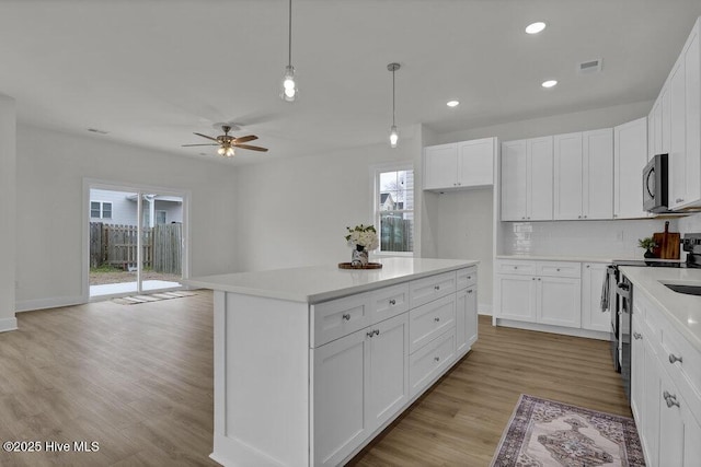 kitchen with pendant lighting, electric stove, white cabinetry, and a kitchen island