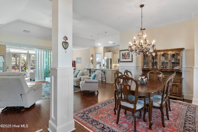 dining space featuring dark hardwood / wood-style flooring, a notable chandelier, crown molding, and ornate columns