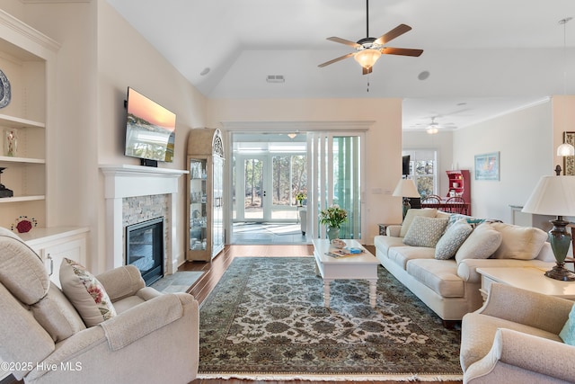 living room with a stone fireplace, vaulted ceiling, ceiling fan, and light wood-type flooring