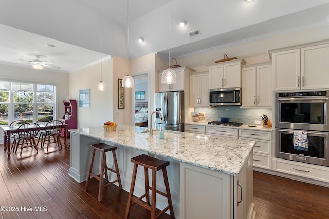 kitchen with hanging light fixtures, stainless steel appliances, dark hardwood / wood-style floors, a center island with sink, and decorative backsplash