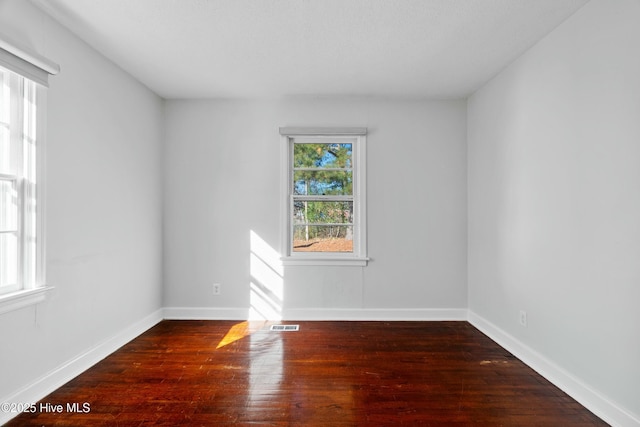 empty room with dark hardwood / wood-style flooring and a healthy amount of sunlight