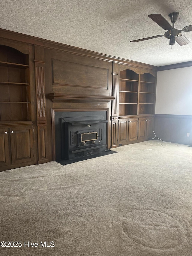 unfurnished living room featuring carpet floors, built in shelves, a textured ceiling, and wainscoting