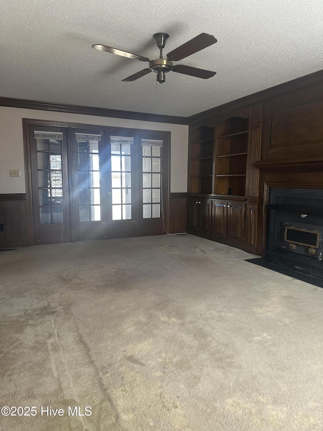 unfurnished living room with a textured ceiling, carpet floors, ornamental molding, and wainscoting