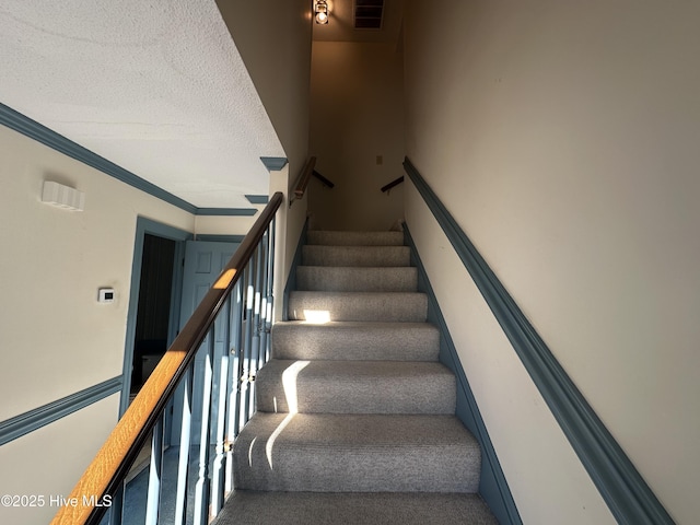 stairs featuring a textured ceiling, carpet, visible vents, and crown molding