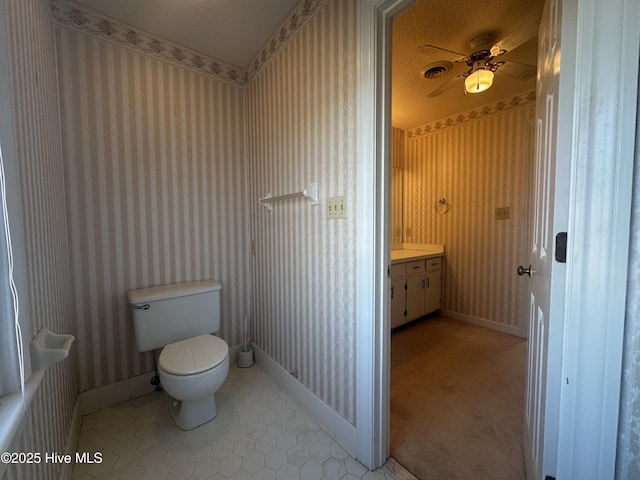 bathroom with baseboards, vanity, toilet, and wallpapered walls