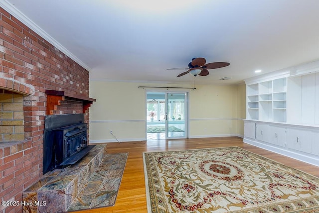 living room with ornamental molding, wood-type flooring, ceiling fan, and a wood stove