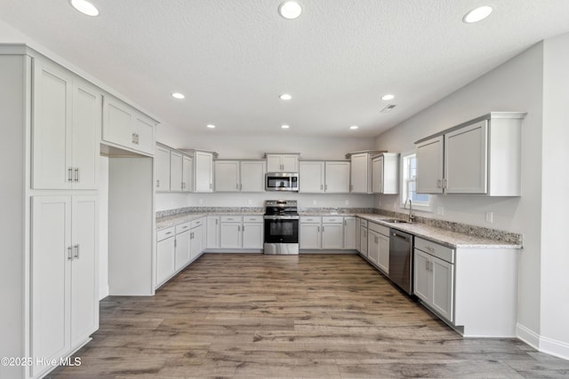 kitchen with sink, stainless steel appliances, a textured ceiling, and light wood-type flooring