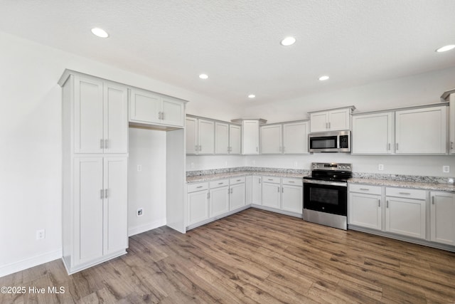 kitchen with appliances with stainless steel finishes, white cabinetry, hardwood / wood-style floors, light stone counters, and a textured ceiling