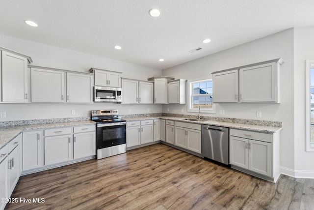 kitchen with sink, dark hardwood / wood-style flooring, light stone counters, stainless steel appliances, and a textured ceiling