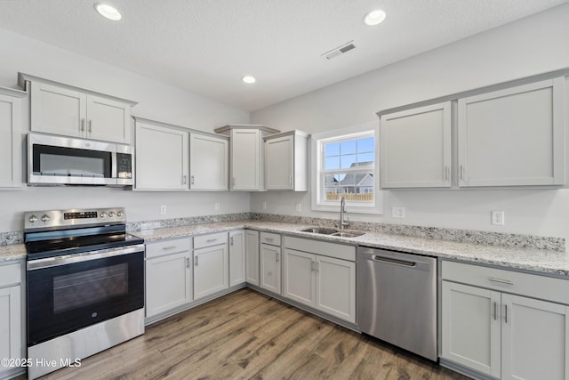 kitchen with wood-type flooring, sink, light stone counters, stainless steel appliances, and a textured ceiling