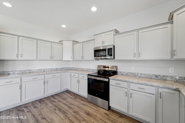 kitchen with appliances with stainless steel finishes, white cabinets, and light wood-type flooring