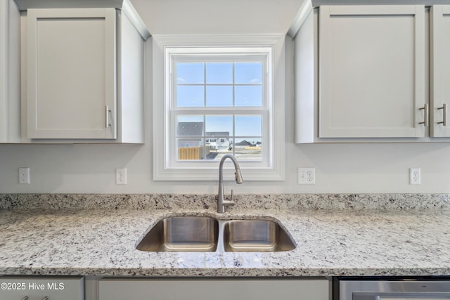 kitchen featuring light stone counters, sink, dishwasher, and white cabinets