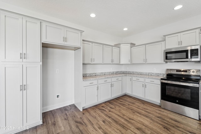 kitchen with white cabinetry, light stone countertops, dark wood-type flooring, and stainless steel appliances