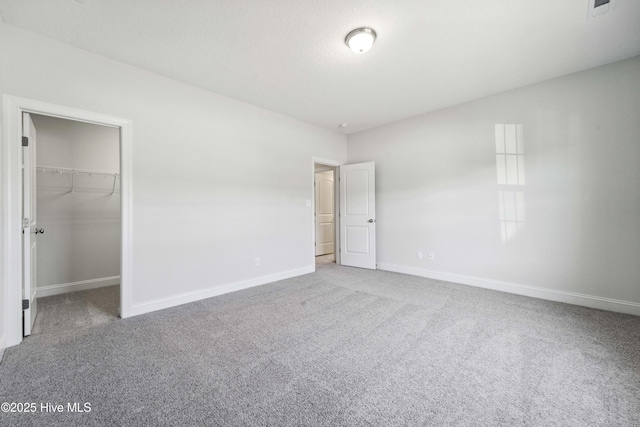 unfurnished bedroom with a walk in closet, carpet floors, a closet, and a textured ceiling