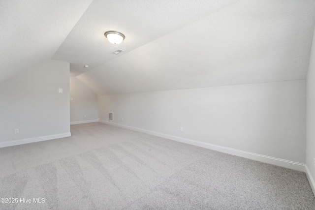 additional living space featuring light colored carpet, lofted ceiling, and a textured ceiling