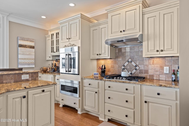 kitchen with crown molding, light hardwood / wood-style flooring, backsplash, stainless steel appliances, and light stone counters