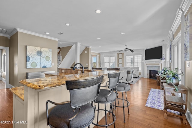 kitchen with ornate columns, ornamental molding, ceiling fan, light hardwood / wood-style floors, and light stone countertops