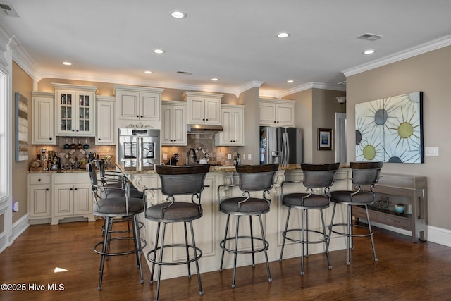 kitchen featuring stainless steel refrigerator with ice dispenser, dark wood-type flooring, a breakfast bar, crown molding, and a center island with sink