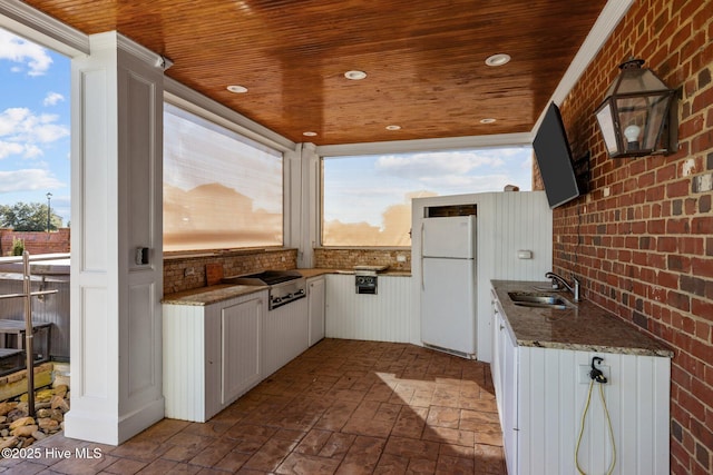 kitchen featuring brick wall, sink, white fridge, and white cabinets