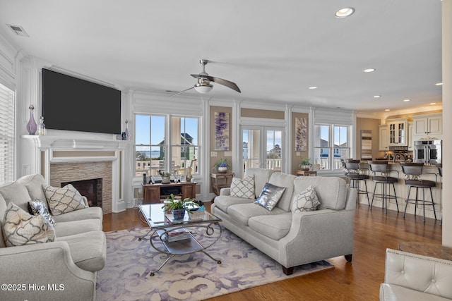 living room featuring a fireplace, wood-type flooring, ornamental molding, and ceiling fan