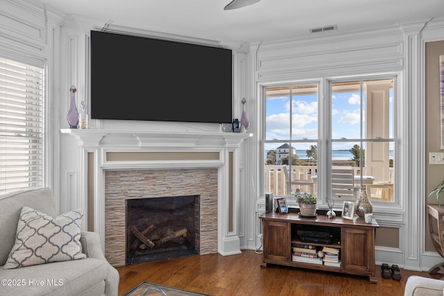 living room with crown molding, a healthy amount of sunlight, dark hardwood / wood-style flooring, and a tiled fireplace