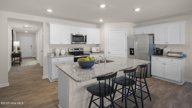 kitchen with a breakfast bar, a center island with sink, dark hardwood / wood-style floors, appliances with stainless steel finishes, and white cabinetry