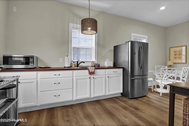 kitchen featuring decorative light fixtures, white cabinetry, wood-type flooring, stainless steel appliances, and sink