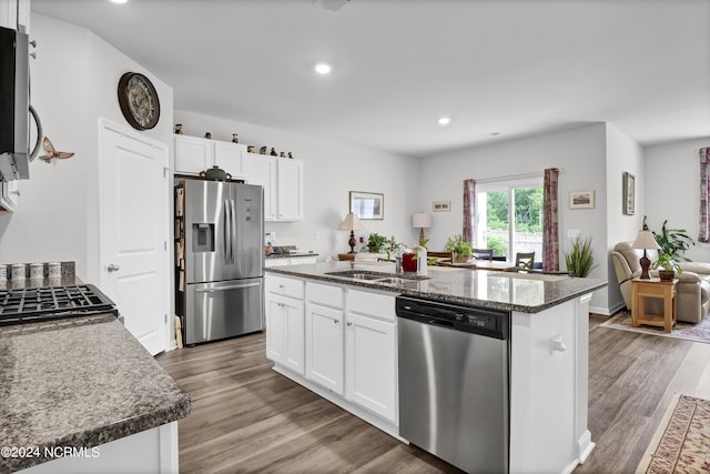 kitchen with dark stone countertops, wood-type flooring, stainless steel appliances, a center island, and white cabinets