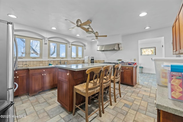 kitchen featuring wall chimney exhaust hood, tasteful backsplash, stainless steel refrigerator, a kitchen breakfast bar, and a kitchen island