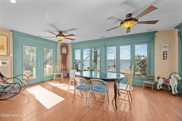 sunroom featuring french doors, ceiling fan, and a water view